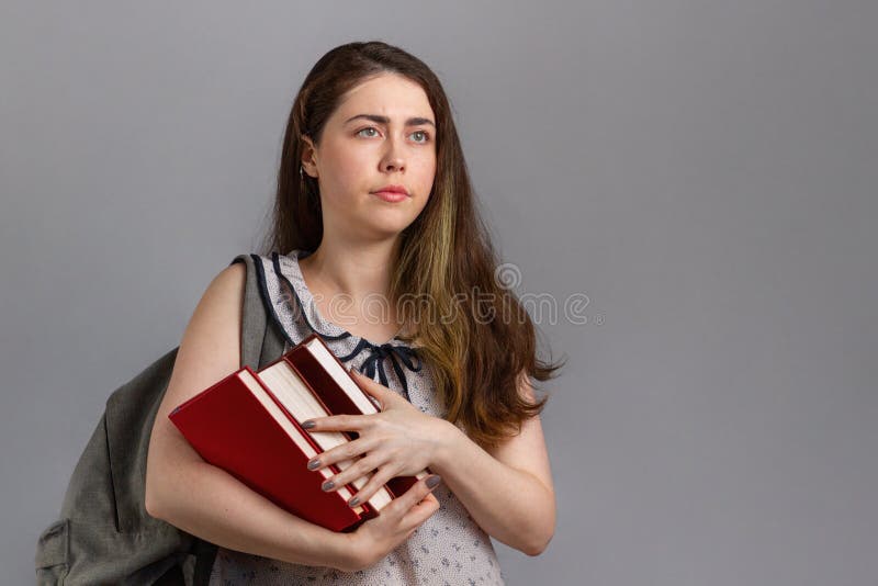 EducaciÃ³n. Una joven con una mochila detrÃ¡s de ella sosteniendo un montÃ³n de libros con una cara descontenta. Copiar espacio