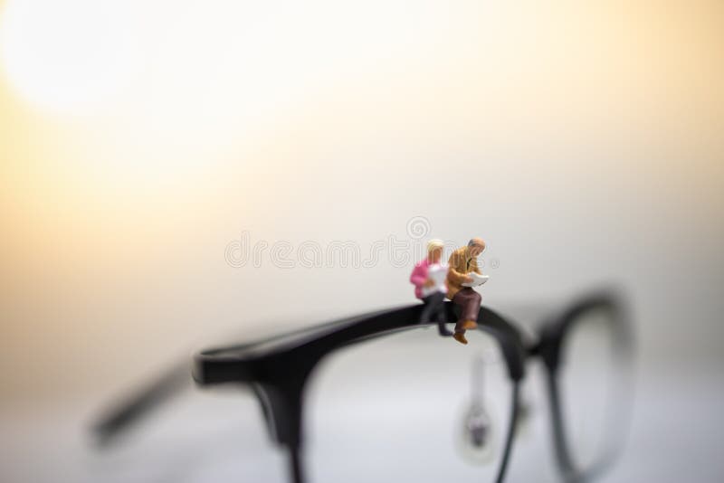 Education and Business Concept. Close up of businessman miniature figures sitting and reading book on reading glasses with copy stock images Education and Business Concept. Close up of businessman miniature figures sitting and reading book on reading glasses with copy stock images