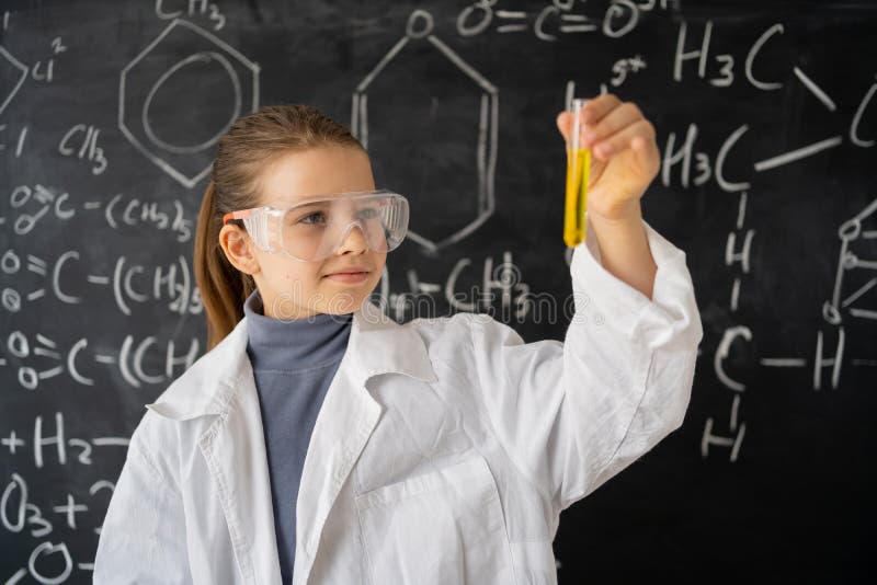 Education concept. little children scientists look at an Erlenmeyer flask containing chemicals to conduct experiments in the laboratory, a student girl in a white coat blackboard background