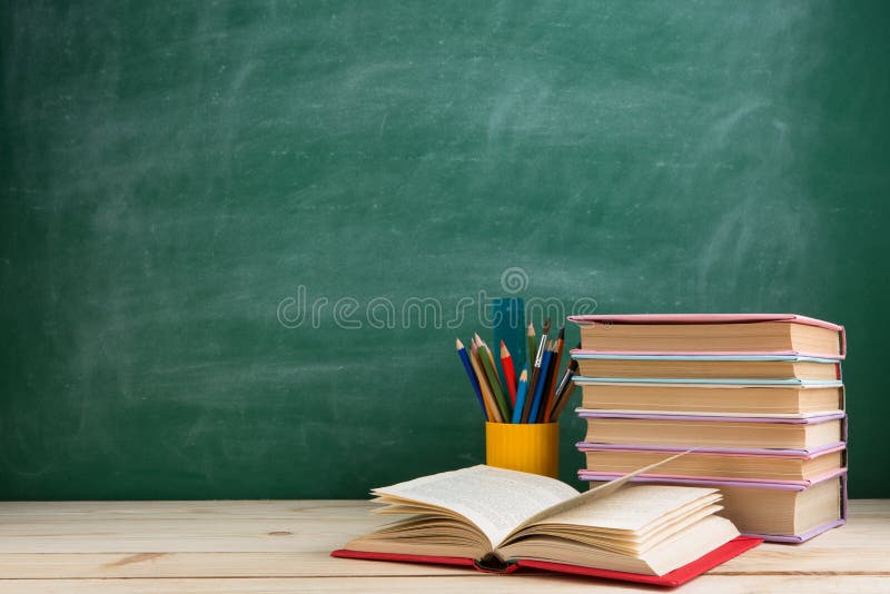 Education and reading concept - group of colorful books on the wooden table in the classroom, blackboard background