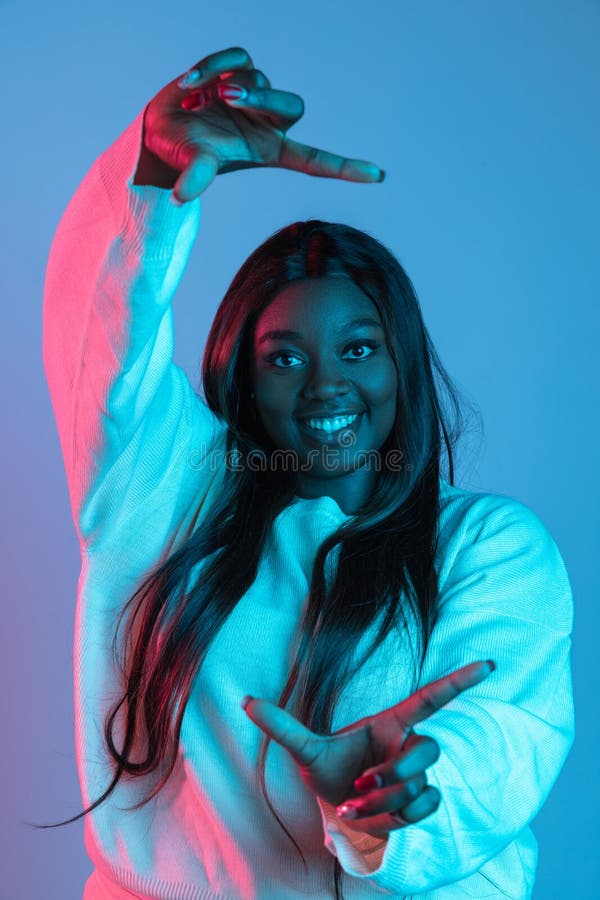 Frame. One African smiling attractive woman with long straight hair isolated on blue background in neon light. Concept of human emotions, facial expression. Bodypositive and diversity. Looks happy. Frame. One African smiling attractive woman with long straight hair isolated on blue background in neon light. Concept of human emotions, facial expression. Bodypositive and diversity. Looks happy