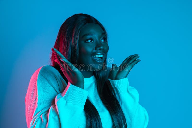 Amazed, delighted. One African beautiful woman with long straight hair isolated on blue studio background in neon light. Concept of human emotions, facial expression. Bodypositive and diversity. Amazed, delighted. One African beautiful woman with long straight hair isolated on blue studio background in neon light. Concept of human emotions, facial expression. Bodypositive and diversity