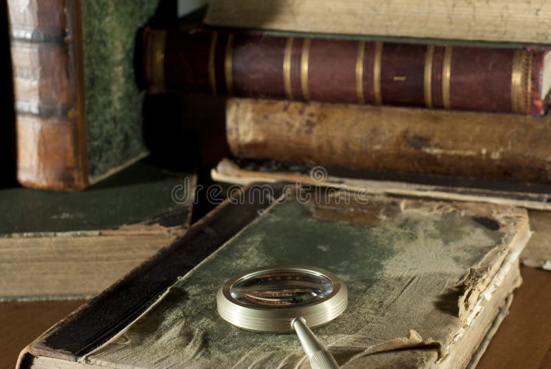 Een antiek boek in een haveloze dekking en een vergrootglas op een vage achtergrond van andere oude boeken royalty-vrije stock afbeelding Een antiek boek in een haveloze dekking en een vergrootglas op een vage achtergrond van andere oude boeken royalty-vrije stock afbeelding