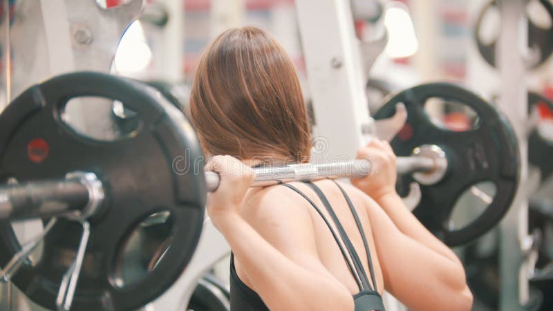 Een atletenvrouw die in de gymnastiek opleiden die - met domoor het hurken op de schouders stock afbeelding Een atletenvrouw die in de gymnastiek opleiden die - met domoor het hurken op de schouders stock afbeelding