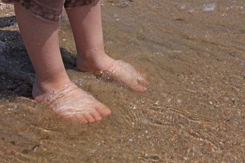 Een baby probeert binnen aan stap aan het zeewater in de eerste keer in een zonnige dag Met onscherpe overzeese achtergrond royalty-vrije stock foto Een baby probeert binnen aan stap aan het zeewater in de eerste keer in een zonnige dag Met onscherpe overzeese achtergrond royalty-vrije stock foto