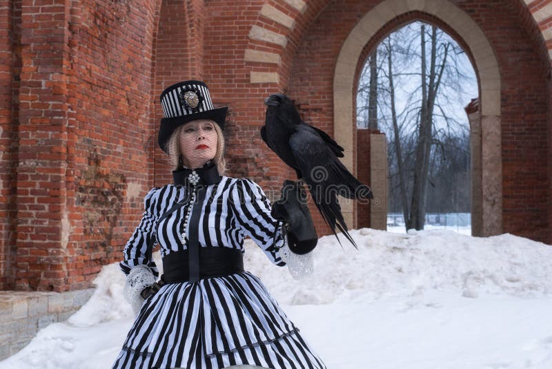 Een bejaarde in een gotische kleding met een zwarte raafhoed op aard in de winter royalty-vrije stock foto's Een bejaarde in een gotische kleding met een zwarte raafhoed op aard in de winter royalty-vrije stock foto's