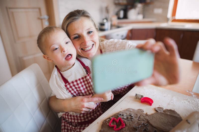 Een benedensyndroomjongen met zijn moeder die binnen selfie wanneer het bakken nemen