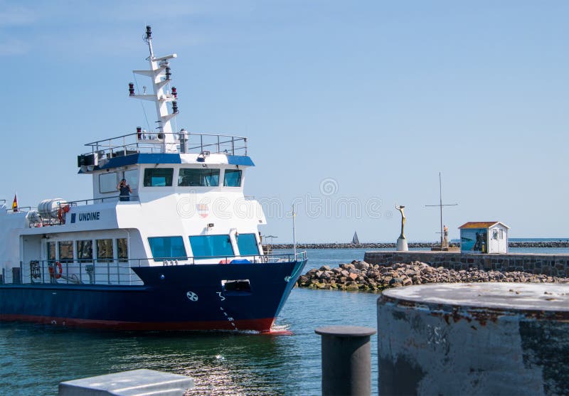 Een boot wordt gezien ingaand Warnemunde-haven, aangezien het een rode vuurtoren en het gouden standbeeld van Esperanda overgaat stock afbeeldingen Een boot wordt gezien ingaand Warnemunde-haven, aangezien het een rode vuurtoren en het gouden standbeeld van Esperanda overgaat stock afbeeldingen