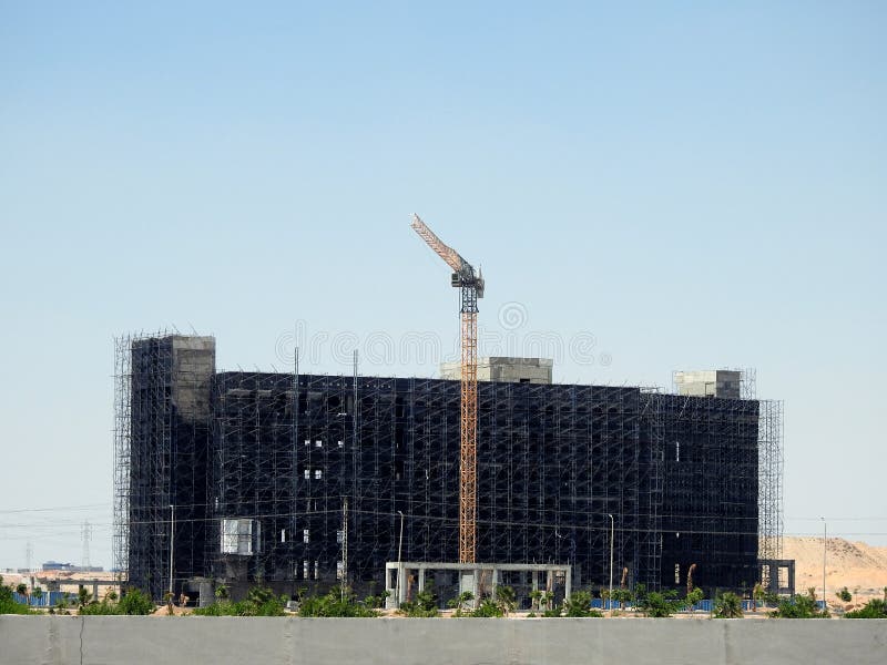 A construction site of a new developmental business building with a crane tower and the cement concrete architecture of the building is surrounded with scaffoldings, new real estate development rise. A construction site of a new developmental business building with a crane tower and the cement concrete architecture of the building is surrounded with scaffoldings, new real estate development rise