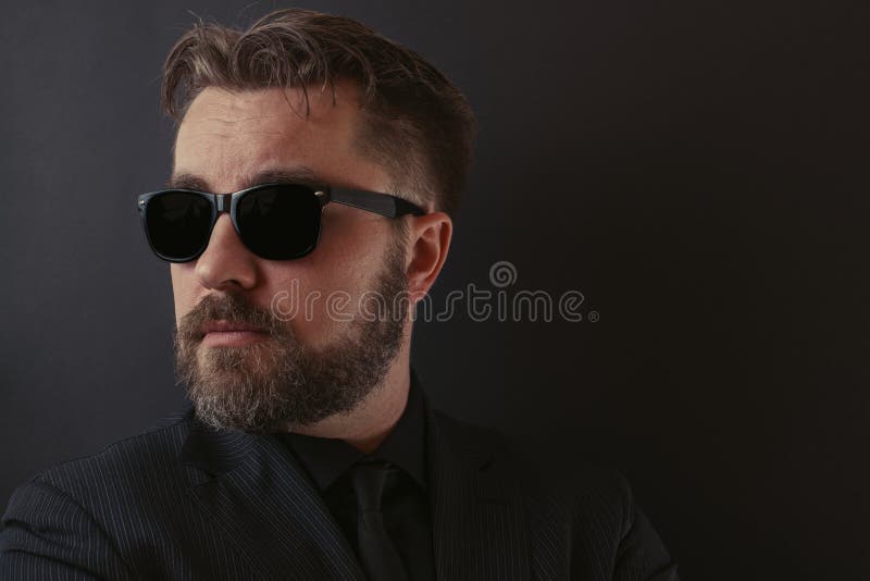 Een brutale mens met een baard en een modieus kapsel in een zwarte passen en zonnebril aan stock fotografie Een brutale mens met een baard en een modieus kapsel in een zwarte passen en zonnebril aan stock fotografie