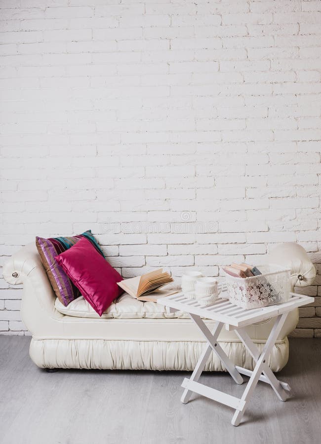 Een deel van binnenland met laag en decoratieve hoofdkussens, witte houten lijst met boeken op het royalty-vrije stock foto Een deel van binnenland met laag en decoratieve hoofdkussens, witte houten lijst met boeken op het royalty-vrije stock foto
