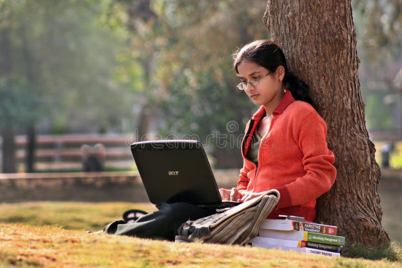 A Young Indian graduating college student studying with books and laptop at the campus ground in India. A Young Indian graduating college student studying with books and laptop at the campus ground in India.