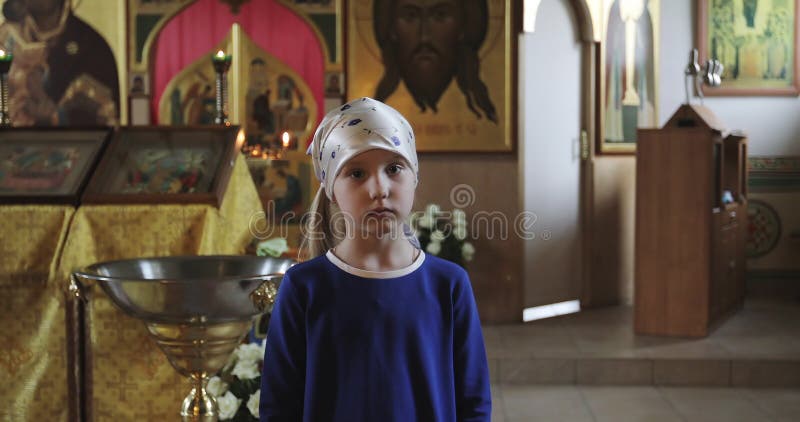 Een droevig meisje in een sjaal en een blauwe kleding bidt in de kerk