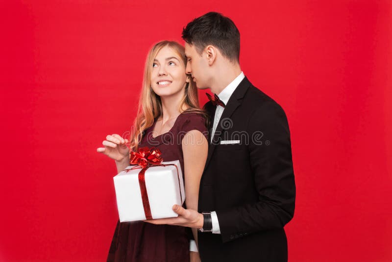Een elegante man in een kostuum geeft een verrassing aan een vrouw, geeft haar een gift, op een rode achtergrond, het concept de royalty-vrije stock afbeelding Een elegante man in een kostuum geeft een verrassing aan een vrouw, geeft haar een gift, op een rode achtergrond, het concept de royalty-vrije stock afbeelding