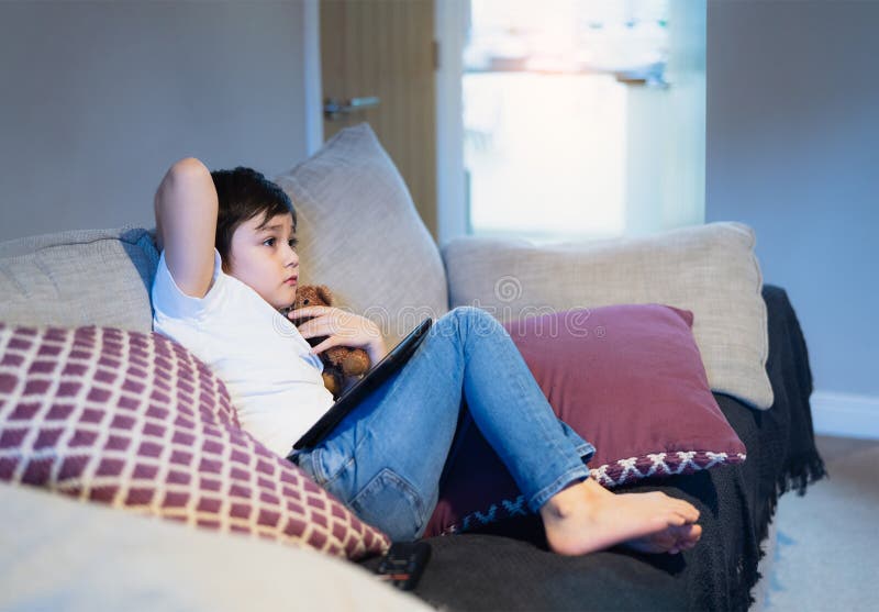 Emotional portrait  kid hugging dog toy sitting on sofa wathcing TV, Young boy siting on couch looking out with thinking face or nervous, Children Health care. Emotional portrait  kid hugging dog toy sitting on sofa wathcing TV, Young boy siting on couch looking out with thinking face or nervous, Children Health care