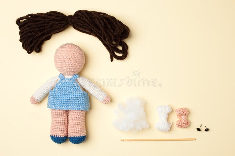 A toy crocheted, a doll in a blue dress, an unfinished work - the hair is not sewn and the decor is not executed, the tools and materials lie nearby. A toy crocheted, a doll in a blue dress, an unfinished work - the hair is not sewn and the decor is not executed, the tools and materials lie nearby