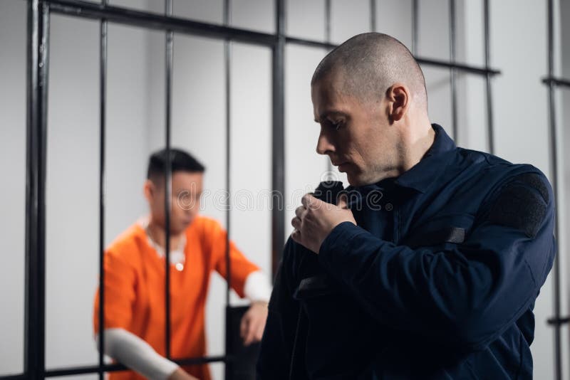 A prison guard in full ammunition communicates with his partner on the radio. In the background, a prisoner in a cell. A prison guard in full ammunition communicates with his partner on the radio. In the background, a prisoner in a cell.