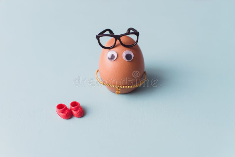 Een grappig leuk bruin ei met zwarte glazen en rode schoenen op blauwe achtergrond stock afbeelding Een grappig leuk bruin ei met zwarte glazen en rode schoenen op blauwe achtergrond stock afbeelding