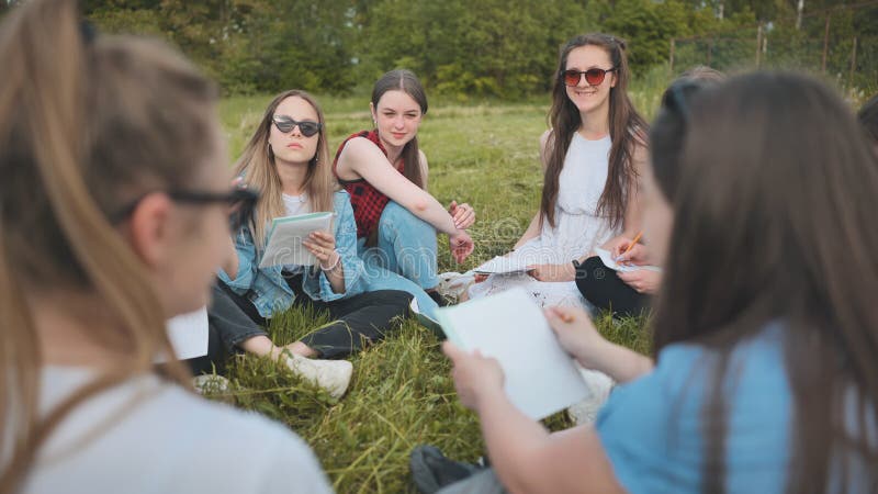 Een groep vrouwelijke studenten zit in een cirkel op een weide voor collectief werk met notebooks.