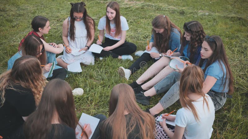 Een groep vrouwelijke studenten zit in een cirkel op een weide voor collectief werk met notebooks.