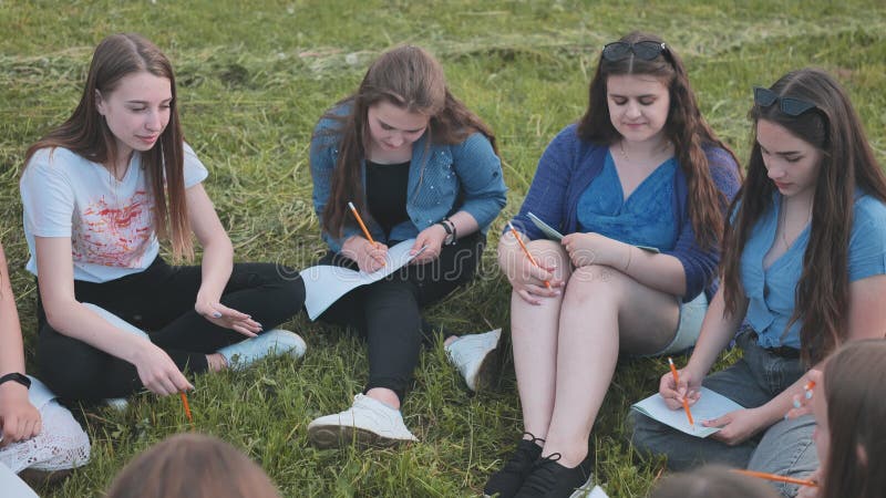 Een groep vrouwelijke studenten zit in een cirkel op een weide voor collectief werk met notebooks.