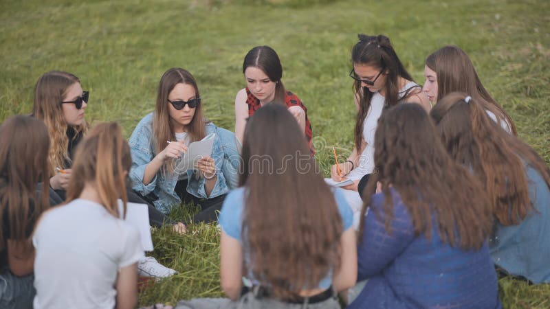 Een groep vrouwelijke studenten zit in een cirkel op een weide voor collectief werk met notebooks.