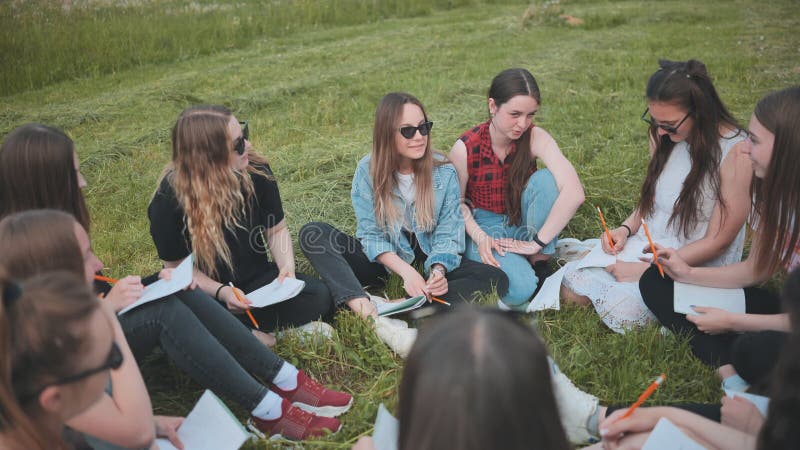 Een groep vrouwelijke studenten zit in een cirkel op een weide voor collectief werk met notebooks.