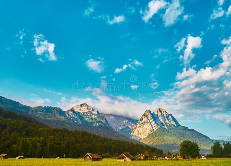 Een heldere blauw-witte hemel met zon en wolken over het massief van de Beierse Alpen voor een bergweide met een bos en royalty-vrije stock fotografie Een heldere blauw-witte hemel met zon en wolken over het massief van de Beierse Alpen voor een bergweide met een bos en royalty-vrije stock fotografie