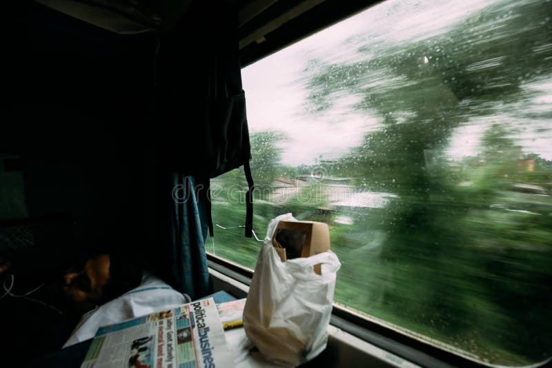 Een Indische kerelslaap met voedsel en krant terwijl een trein die zich met het groene onduidelijke beeld van de boommotie in de stock fotografie Een Indische kerelslaap met voedsel en krant terwijl een trein die zich met het groene onduidelijke beeld van de boommotie in de stock fotografie
