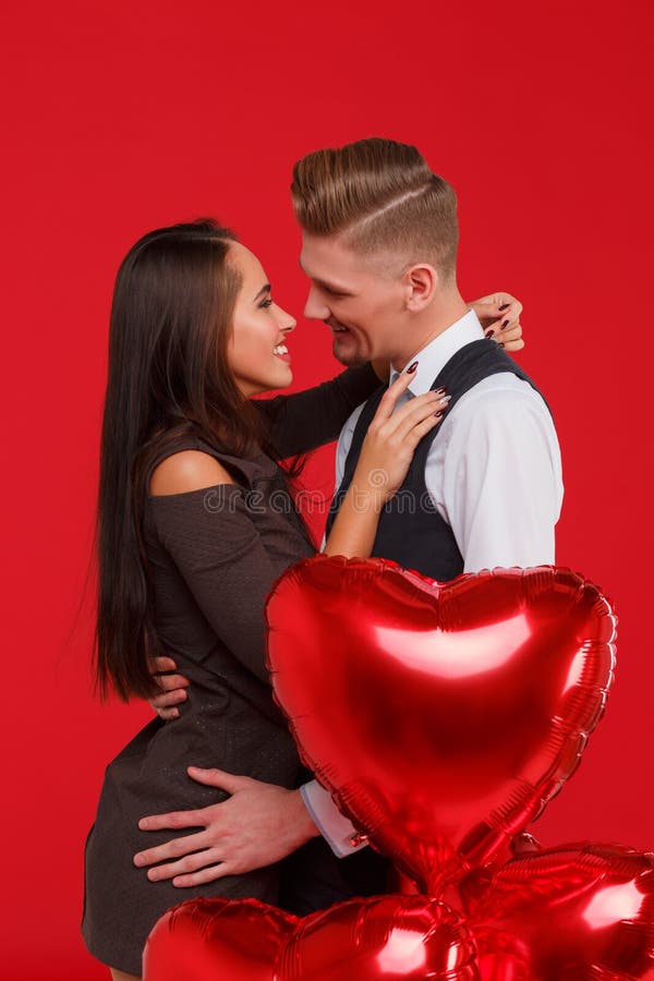 Een jong en mooi paar die en elkaar met rode luchtballons kussen koesteren in een hartvorm, de Dag van Valentine ` s royalty-vrije stock afbeeldingen Een jong en mooi paar die en elkaar met rode luchtballons kussen koesteren in een hartvorm, de Dag van Valentine ` s royalty-vrije stock afbeeldingen