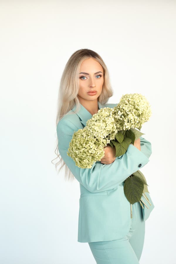 Young beautiful blonde woman with long hair in mint green pantsuit with armful of hydrangeas flowers in arms. Portrait. Young beautiful blonde woman with long hair in mint green pantsuit with armful of hydrangeas flowers in arms. Portrait