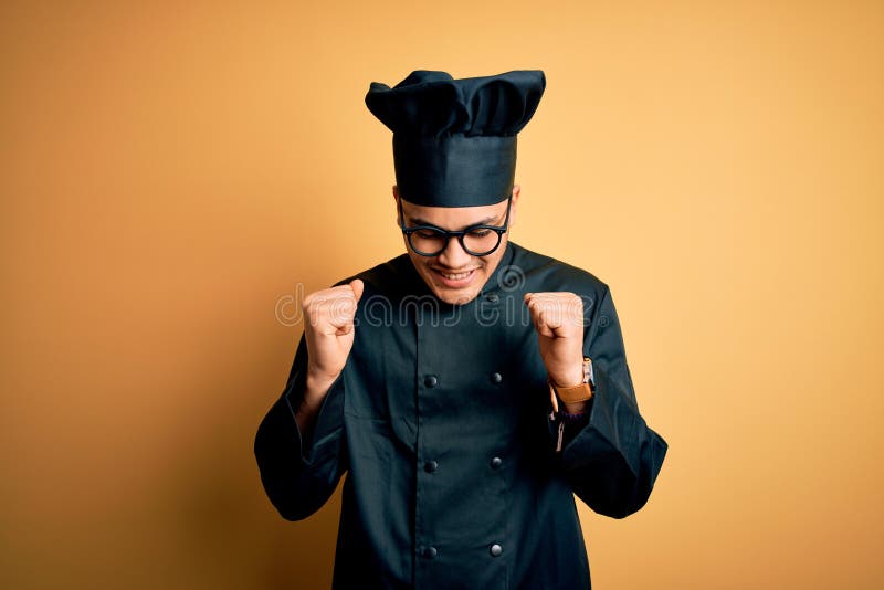 Young brazilian chef man wearing cooker uniform and hat over isolated yellow background excited for success with arms raised and eyes closed celebrating victory smiling. Winner concept. Young brazilian chef man wearing cooker uniform and hat over isolated yellow background excited for success with arms raised and eyes closed celebrating victory smiling. Winner concept