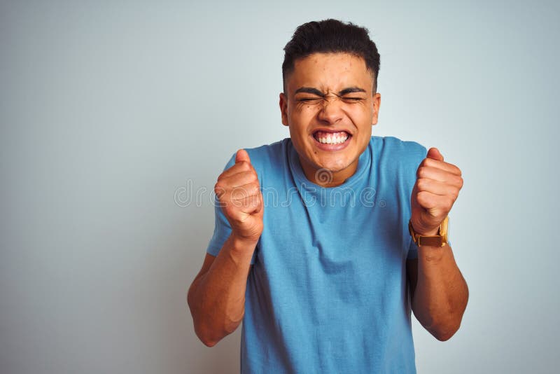 Young brazilian man wearing blue t-shirt standing over isolated white background excited for success with arms raised and eyes closed celebrating victory smiling. Winner concept. Young brazilian man wearing blue t-shirt standing over isolated white background excited for success with arms raised and eyes closed celebrating victory smiling. Winner concept