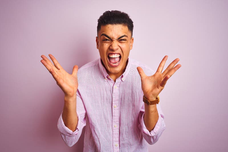 Young brazilian man wearing shirt standing over isolated pink background celebrating crazy and amazed for success with arms raised and open eyes screaming excited. Winner concept. Young brazilian man wearing shirt standing over isolated pink background celebrating crazy and amazed for success with arms raised and open eyes screaming excited. Winner concept