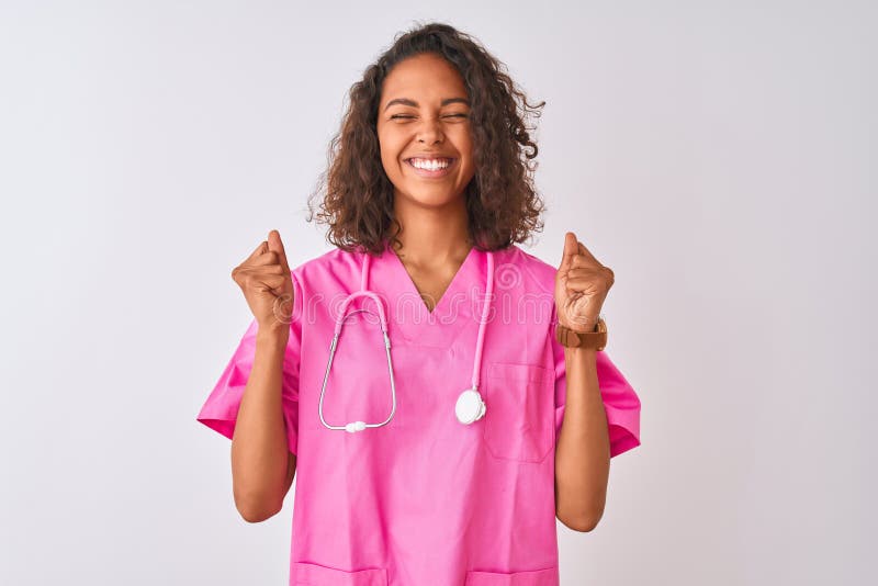 Young brazilian nurse woman wearing stethoscope standing over isolated white background excited for success with arms raised and eyes closed celebrating victory smiling. Winner concept. Young brazilian nurse woman wearing stethoscope standing over isolated white background excited for success with arms raised and eyes closed celebrating victory smiling. Winner concept