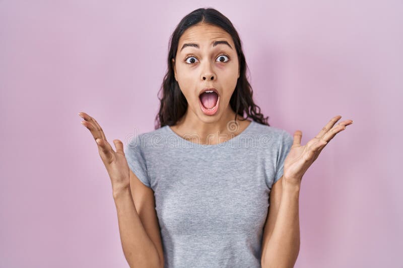 Young brazilian woman wearing casual t shirt over pink background celebrating crazy and amazed for success with arms raised and open eyes screaming excited. winner concept. Young brazilian woman wearing casual t shirt over pink background celebrating crazy and amazed for success with arms raised and open eyes screaming excited. winner concept