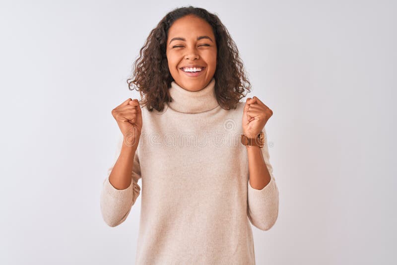 Young brazilian woman wearing turtleneck sweater standing over isolated white background excited for success with arms raised and eyes closed celebrating victory smiling. Winner concept. Young brazilian woman wearing turtleneck sweater standing over isolated white background excited for success with arms raised and eyes closed celebrating victory smiling. Winner concept