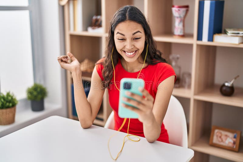 Young brazilian woman doing video call with smartphone screaming proud, celebrating victory and success very excited with raised arm. Young brazilian woman doing video call with smartphone screaming proud, celebrating victory and success very excited with raised arm