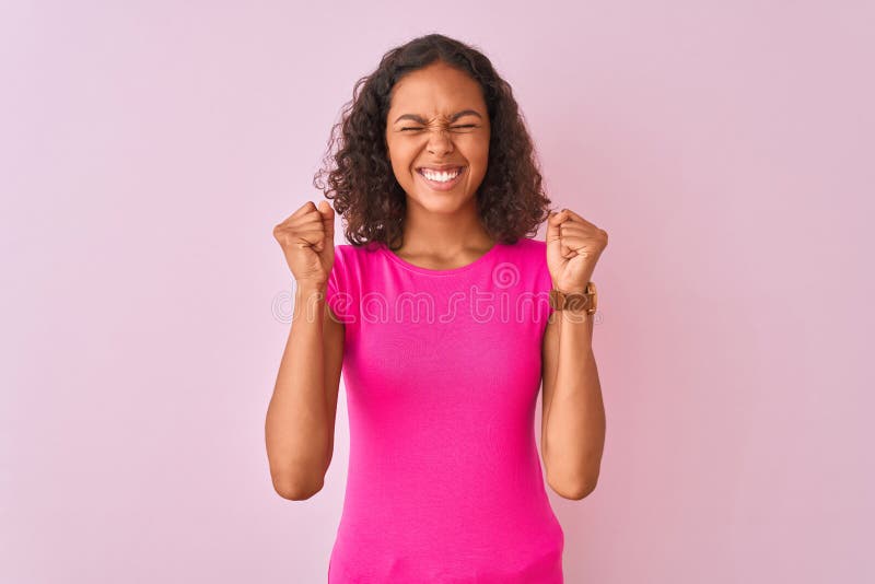 Young brazilian woman wearing t-shirt standing over isolated pink background excited for success with arms raised and eyes closed celebrating victory smiling. Winner concept. Young brazilian woman wearing t-shirt standing over isolated pink background excited for success with arms raised and eyes closed celebrating victory smiling. Winner concept