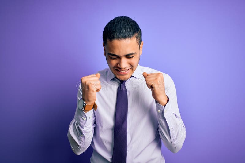 Young brazilian businessman wearing elegant tie standing over isolated purple background excited for success with arms raised and eyes closed celebrating victory smiling. Winner concept. Young brazilian businessman wearing elegant tie standing over isolated purple background excited for success with arms raised and eyes closed celebrating victory smiling. Winner concept