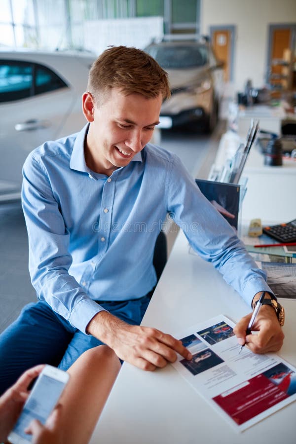 Een jonge kerel die documenten in de toonzaal ondertekenen om een nieuwe auto te kopen royalty-vrije stock afbeelding Een jonge kerel die documenten in de toonzaal ondertekenen om een nieuwe auto te kopen royalty-vrije stock afbeelding