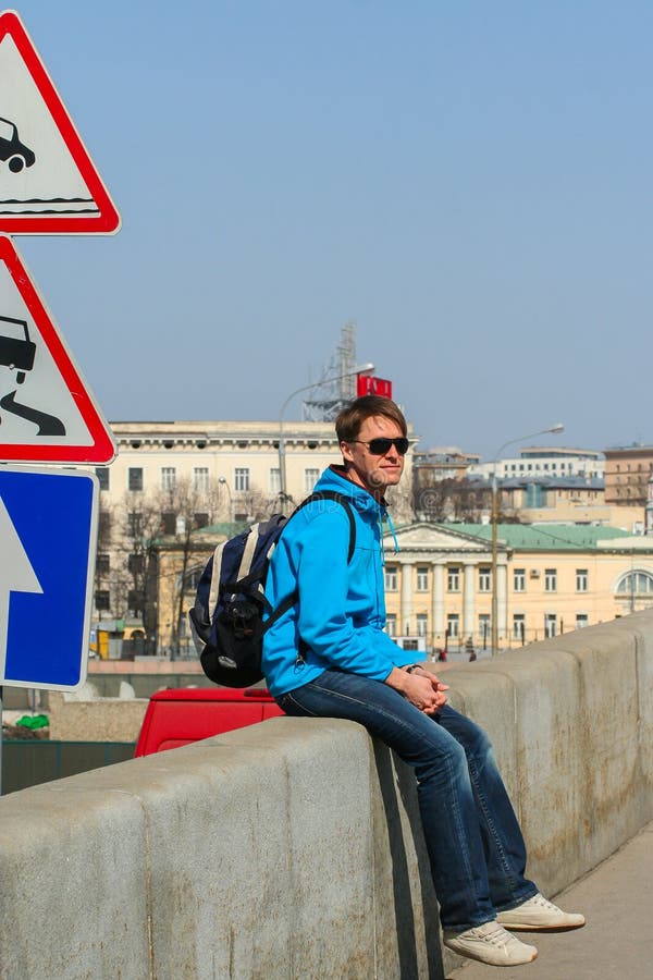 Een jonge mens die zonnebril dragen en op de brug door verkeersteken zitten stock foto's Een jonge mens die zonnebril dragen en op de brug door verkeersteken zitten stock foto's