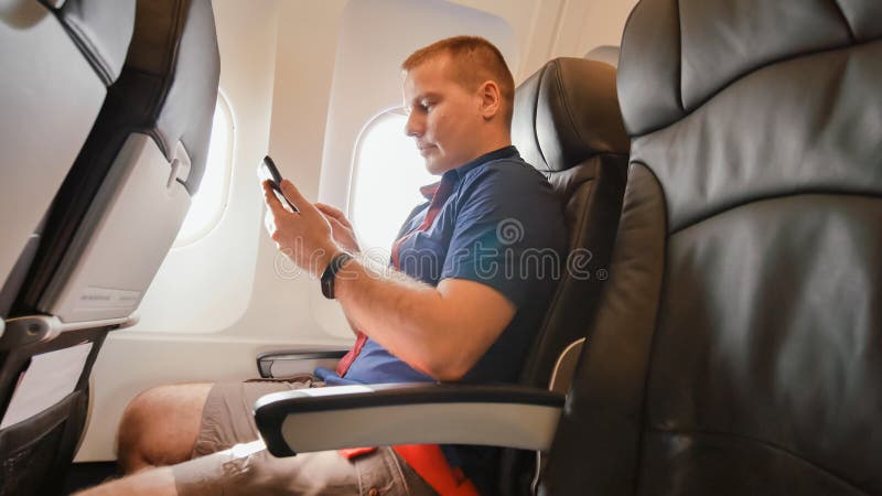 A young man in an airplane before a flight communicates on a mobile phone. A young man in an airplane before a flight communicates on a mobile phone