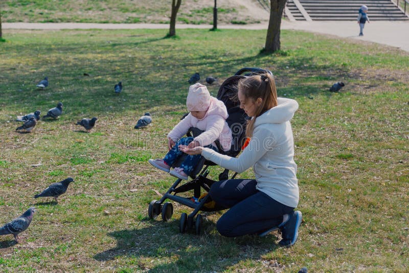 Een jonge moeder met een baby in een kinderwagen voedt duiven royalty-vrije stock afbeelding Een jonge moeder met een baby in een kinderwagen voedt duiven royalty-vrije stock afbeelding