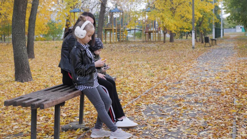 Een jonge moeder met twee kinderen op een bank in het herfstpark Een vriendelijk gezinsconcept