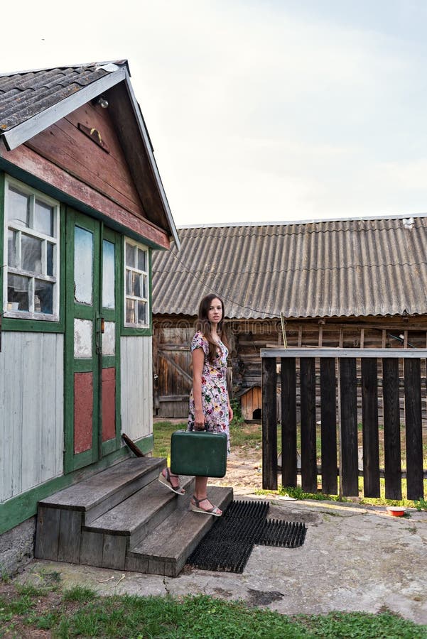 Een jonge slanke vrouw in een uitstekende kleding daalt de stappen van een dorps sjofel huis aan een werf van het land met loodse stock fotografie Een jonge slanke vrouw in een uitstekende kleding daalt de stappen van een dorps sjofel huis aan een werf van het land met loodse stock fotografie