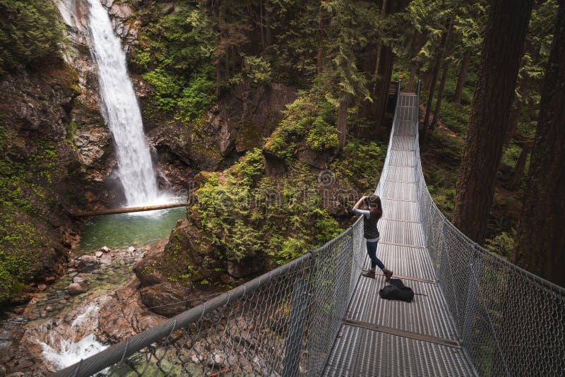 Een jonge vrouw op een hangbrug die een foto van een waterval nemen royalty-vrije stock afbeeldingen Een jonge vrouw op een hangbrug die een foto van een waterval nemen royalty-vrije stock afbeeldingen