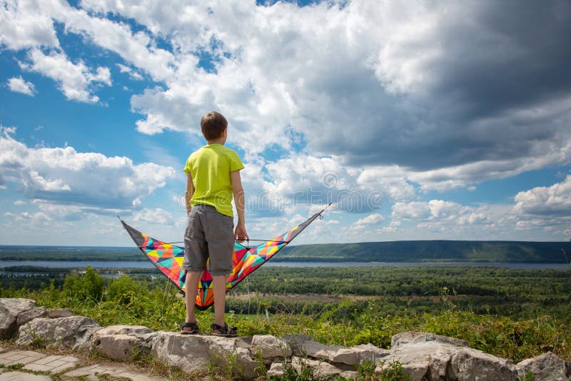 Een jongen met een kleurrijke vlieger in zijn handen tegen de blauwe hemel met wolken Een kind in een gele T-shirt en borrels Moo royalty-vrije stock foto's Een jongen met een kleurrijke vlieger in zijn handen tegen de blauwe hemel met wolken Een kind in een gele T-shirt en borrels Moo royalty-vrije stock foto's