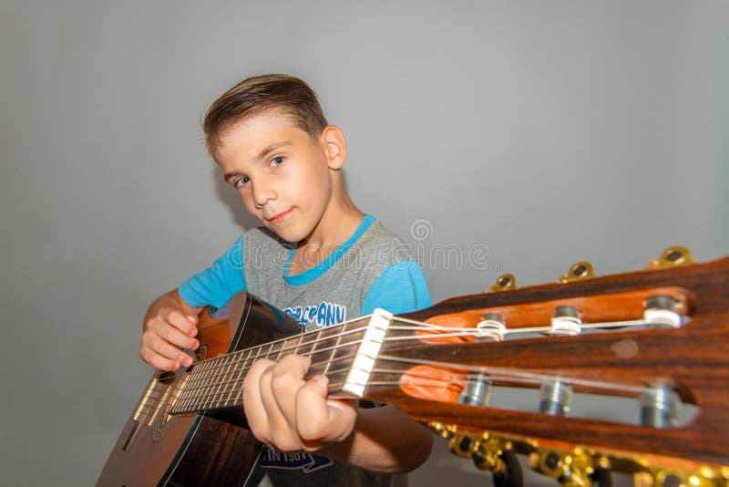 Een jongen speelt de gitaar op een grijze achtergrond in de studio, de brede foto van het hoekclose-up royalty-vrije stock foto Een jongen speelt de gitaar op een grijze achtergrond in de studio, de brede foto van het hoekclose-up royalty-vrije stock foto