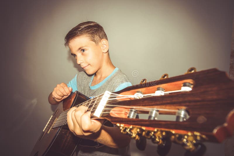 Een jongen speelt de gitaar op een grijze achtergrond in de studio, de brede foto van het hoekclose-up royalty-vrije stock foto Een jongen speelt de gitaar op een grijze achtergrond in de studio, de brede foto van het hoekclose-up royalty-vrije stock foto